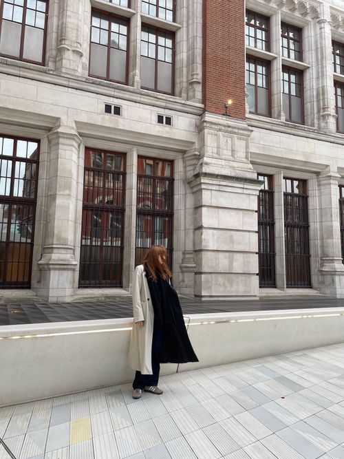 Free Woman in a coat standing by a grand London building, showcasing urban fashion. Stock Photo