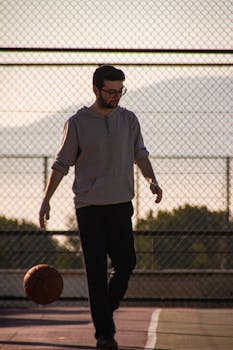 Man playing basketball outdoors casually on a court at sunset, enjoying leisure time.