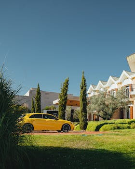 Elegant house with a yellow sports car in the garden, surrounded by greenery on a sunny day.
