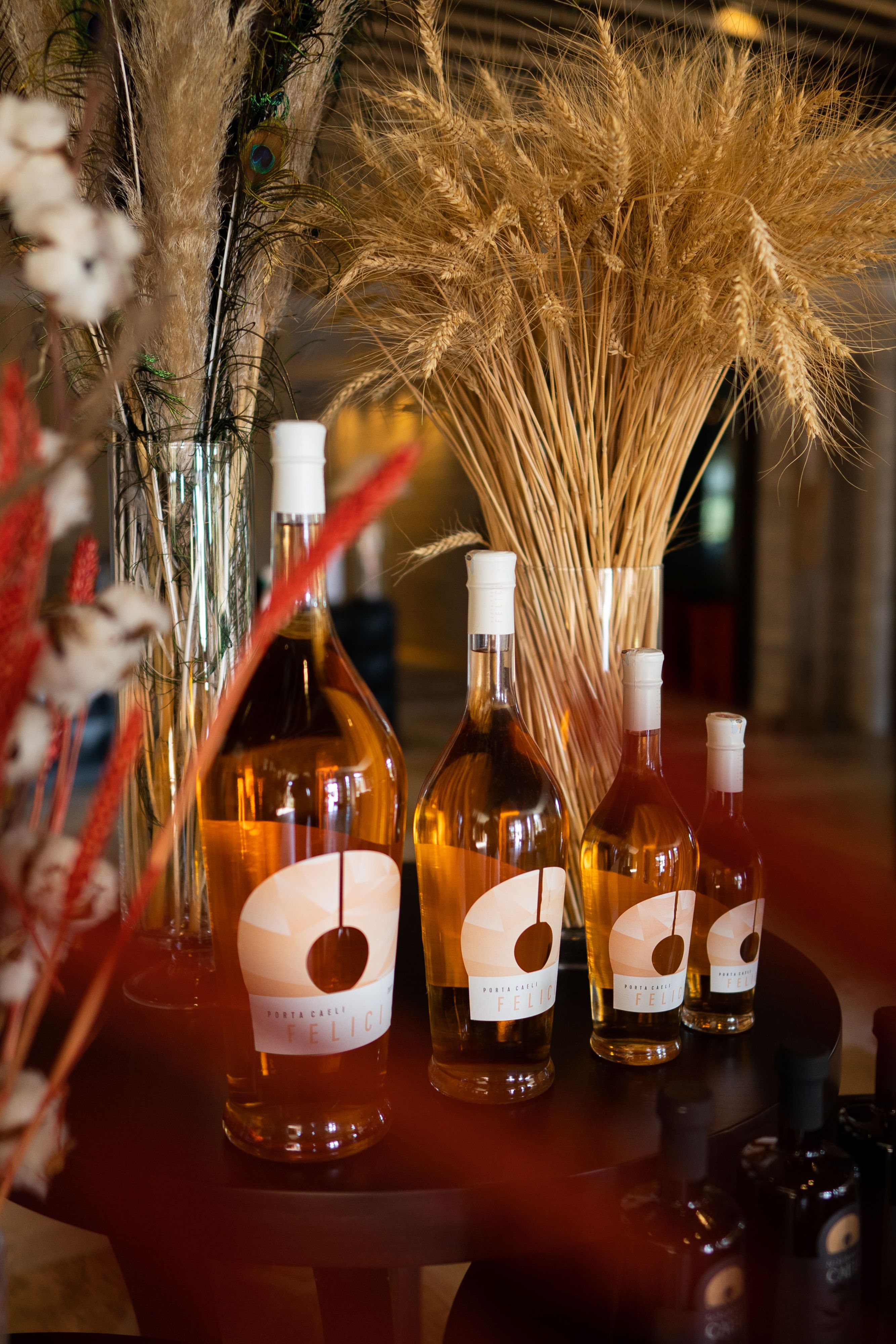 Stylish display of wine bottles with dried wheat arrangement in a Çanakkale setting.