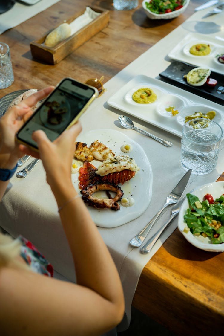 Woman Taking Pictures Of Food On Table