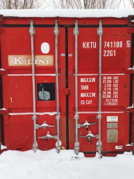 Red shipping container with visible text in snowy Karaganda, Kazakhstan setting.