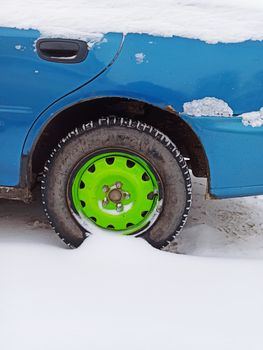 A vibrant green wheel on a blue car covered in snow, showcasing winter conditions.