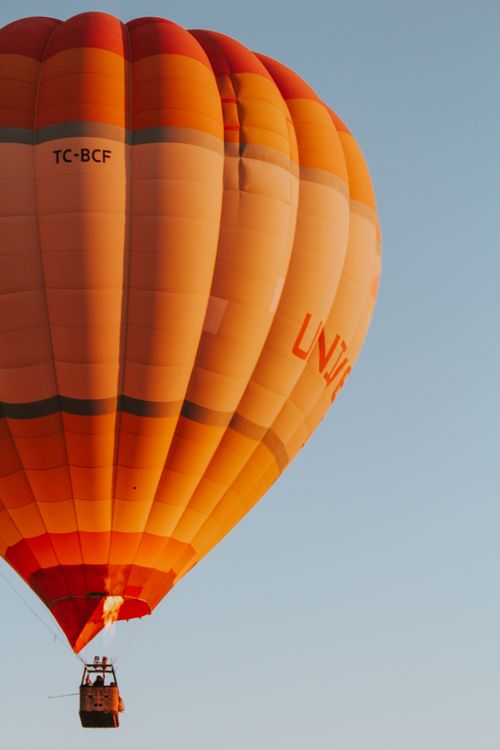 Free Vibrant orange hot air balloon floating in the clear blue sky in Turkey during the day. Stock Photo