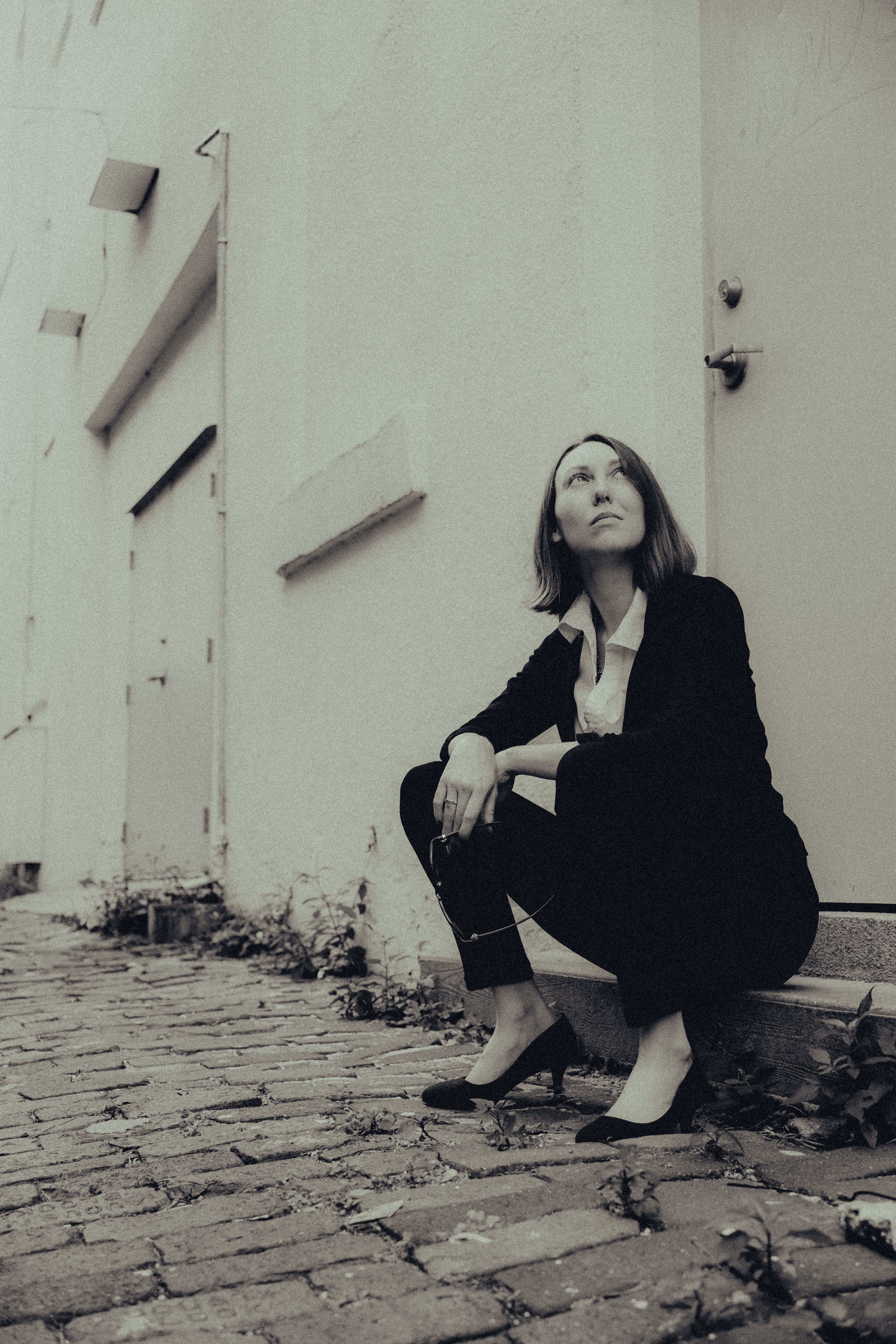 Fashionably dressed woman sits in a city alley, exuding modern elegance.