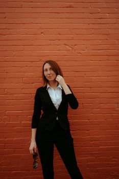 Confident woman in formal business attire posing against a brick wall.