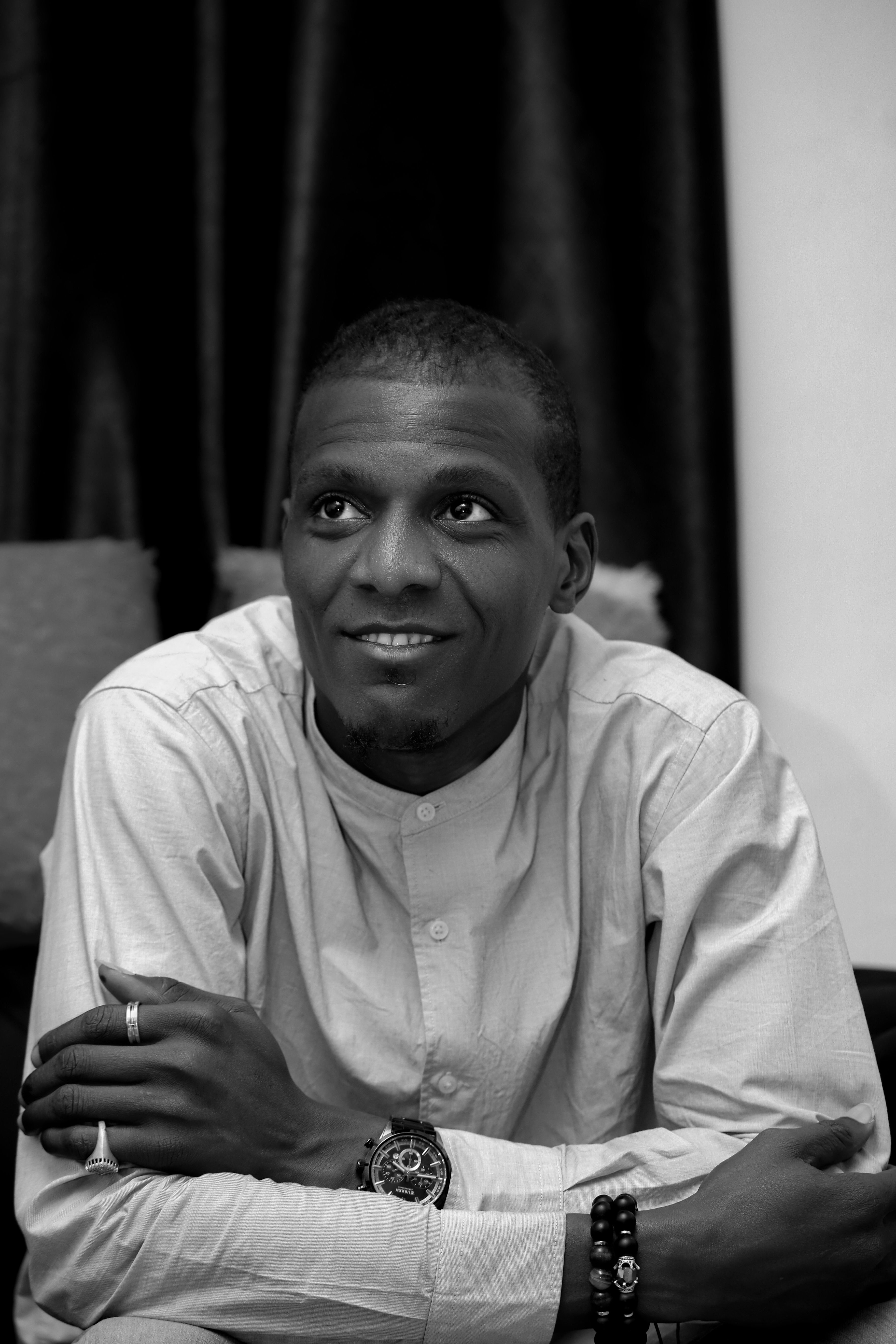 Black and white portrait of a smiling man with crossed arms indoors.