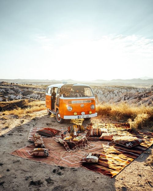Free A vibrant picnic setup with a vintage orange van overlooking Cappadocia's unique landscape under bright sunlight. Stock Photo