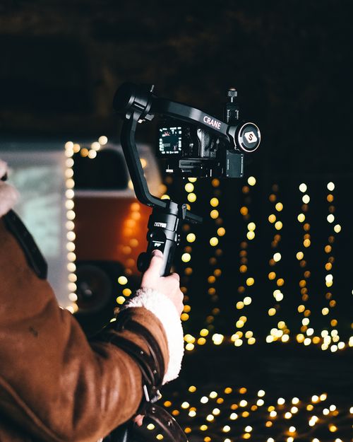 Free Person holding a camera gimbal with bokeh lights in the background, creating a festive atmosphere. Stock Photo