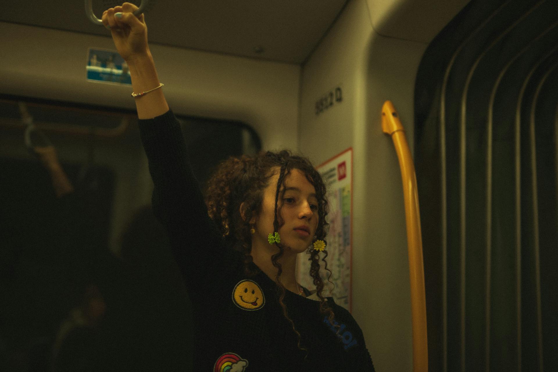 A girl with curly hair holding a handle on a Milan metro train, standing inside.