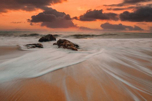 Breathtaking view of the ocean waves and rocks during a warm sunset.