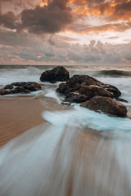 Free Stunning long exposure capture of waves over rocks at sunset on a sandy beach. Stock Photo