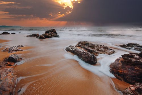 Free A captivating seascape at sunset, showcasing dramatic skies and gentle waves over rocky shorelines. Stock Photo