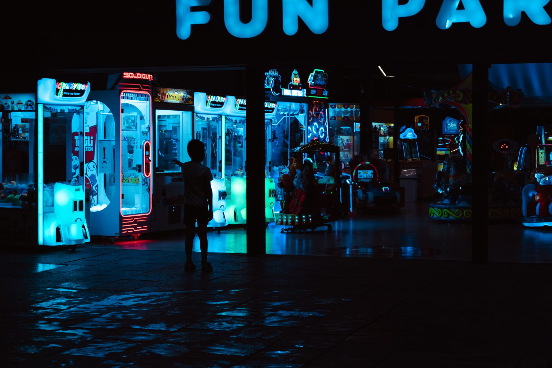 A silhouetted child stands before illuminated arcade machines at night, capturing a nostalgic funfair atmosphere.
