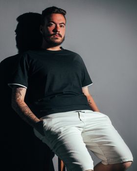 Man sitting confidently with hands in pockets, casting shadow on wall.