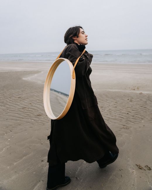 Artistic fashion portrait of a woman carrying a mirror on a serene beach.