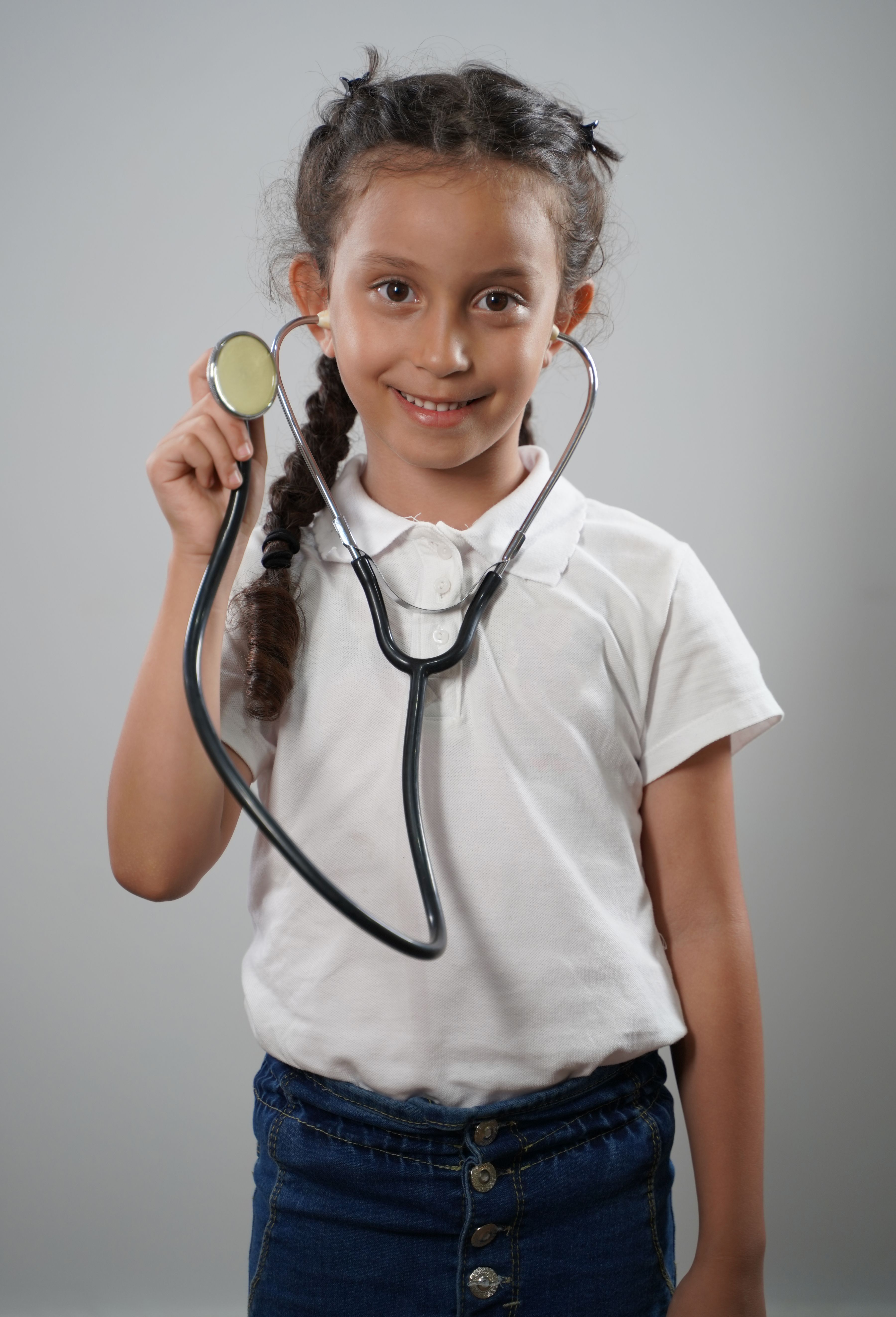 Young girl smiling while holding a stethoscope, pretending to be a doctor.