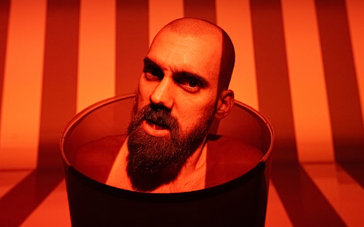 Red Toned Photo Of A Bald Bearded Man Performing Being Imprisoned