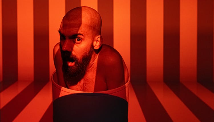 Red Toned Photo Of A Bald Bearded Man Performing Being Imprisoned