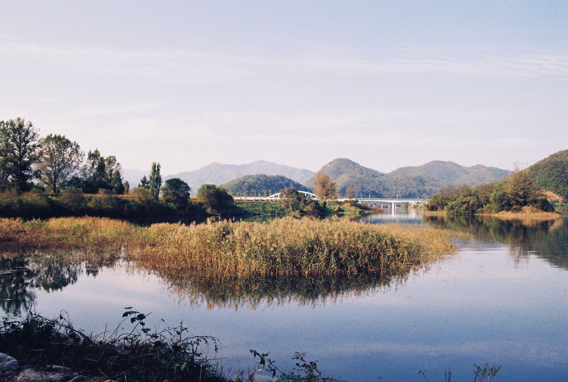 Tranquil landscape of a mountain lake with a bridge, reflections, and lush greenery.