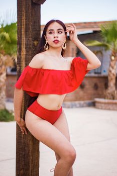 Stylish woman in a red bikini standing by a wooden post in Ciudad Juárez.