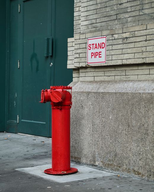 A red standpipe against a building wall on a city sidewalk.