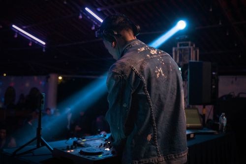 Free DJ performing music in a dimly lit nightclub with blue stage lights. Stock Photo