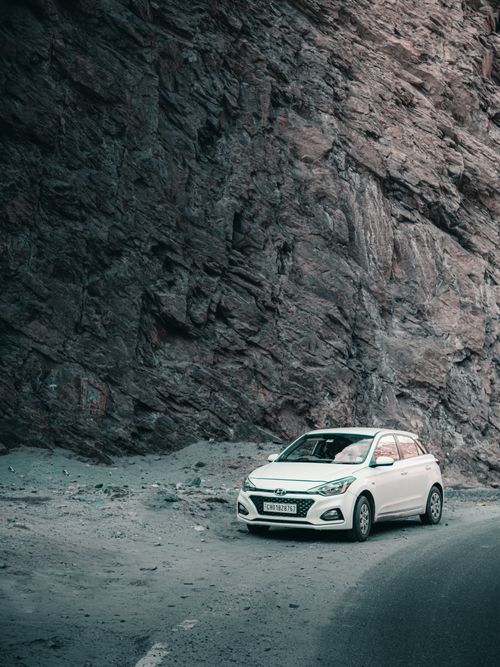 Free A white car parked on a dirt road next to a rocky cliff, depicting a travel and adventure scene. Stock Photo