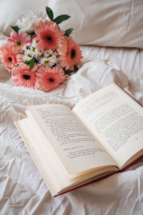 Free Open book on white linen with a bouquet of pink flowers, creating a soft and relaxing ambiance. Stock Photo