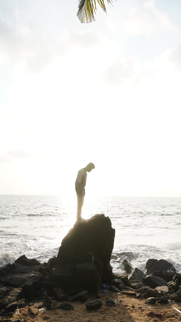 Sunlight Over Man Standing On Rock On Sea Shore