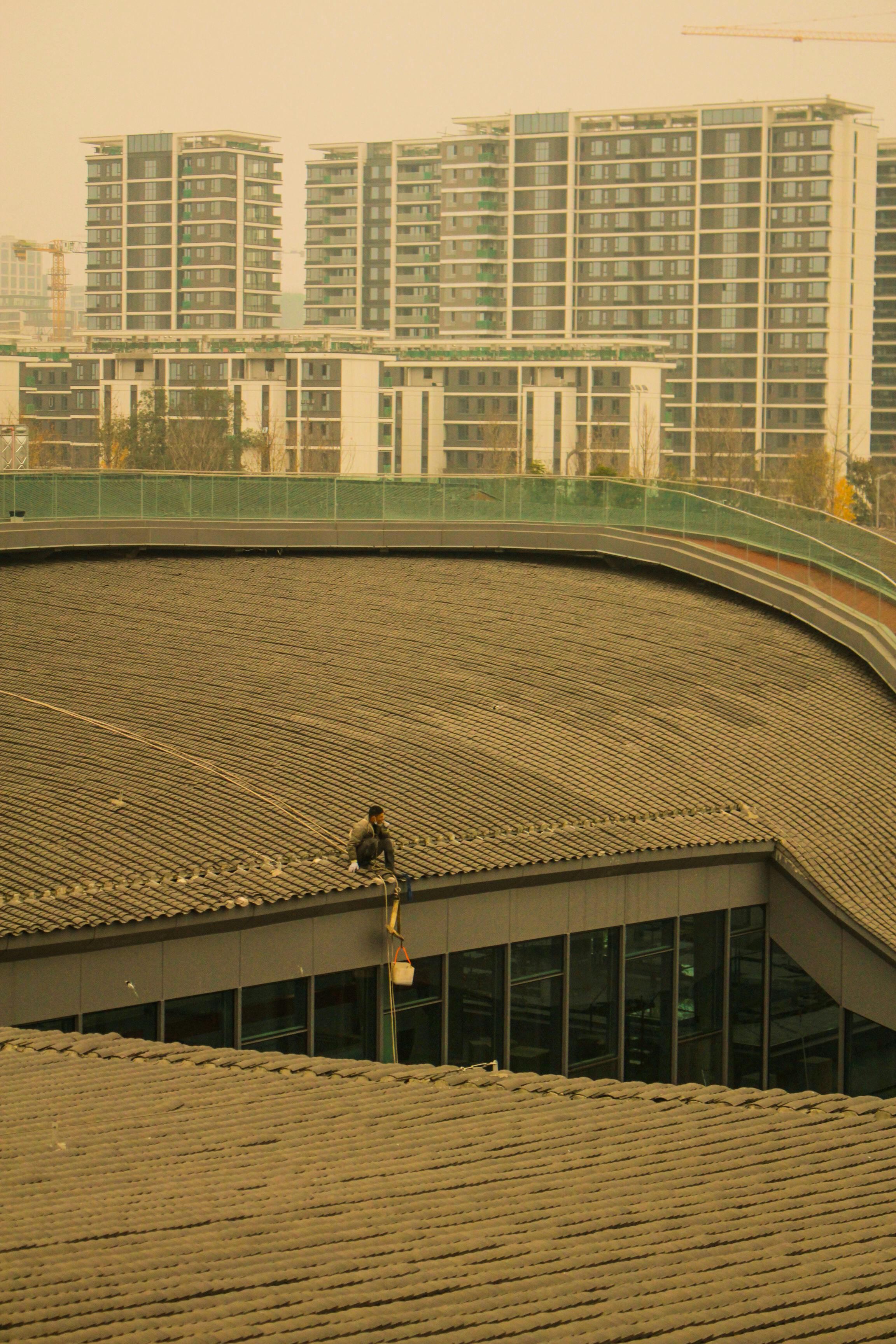 A worker sits on a rooftop against a backdrop of modern high-rises in Chengdu, China