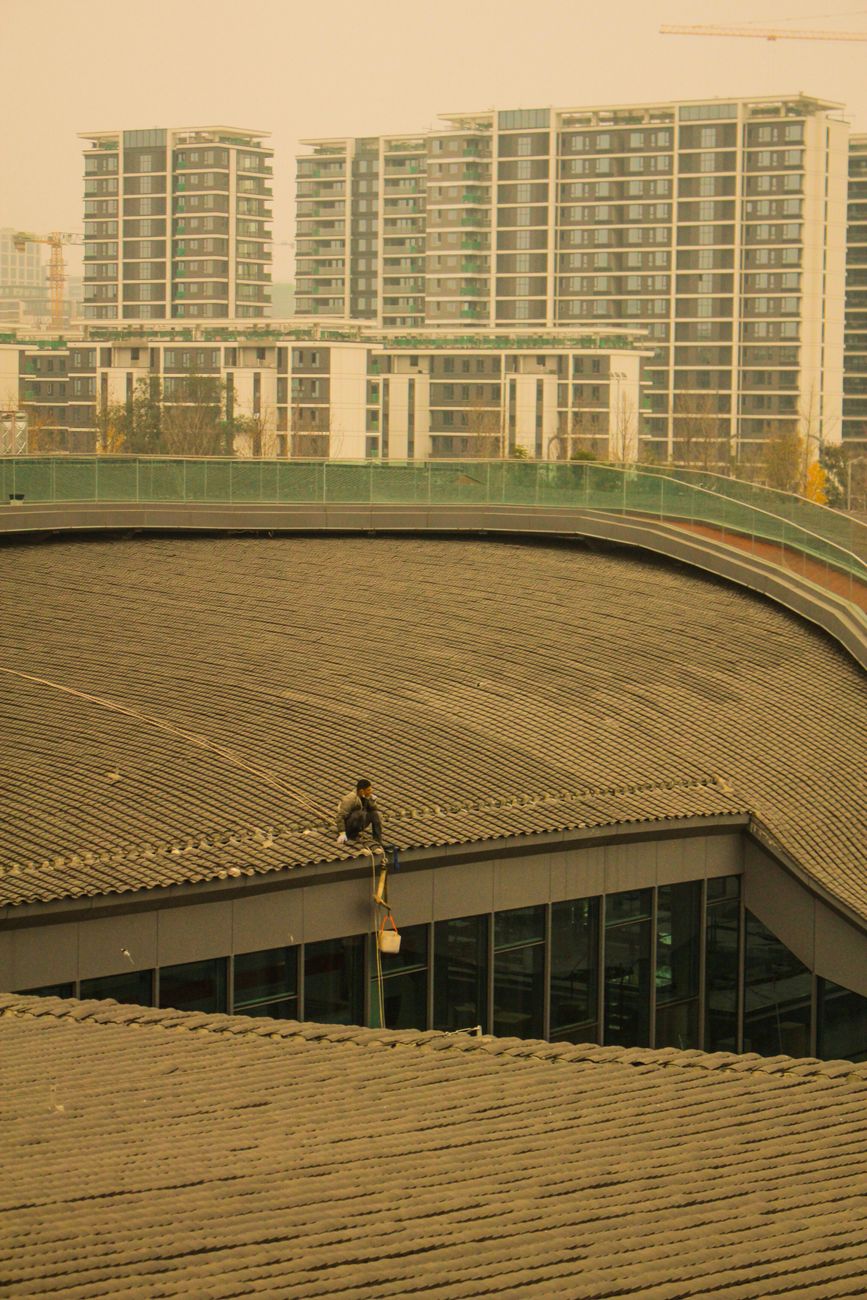 A worker sits on a rooftop against a backdrop of modern high-rises in Chengdu, China