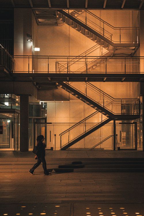 Free A person walking past a lit modern building facade at night. Stock Photo