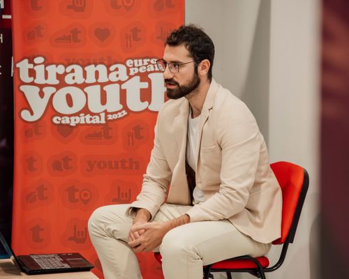 Free Man sitting at the Tirana Youth Capital 2022 event, wearing a blazer and eyeglasses. Stock Photo