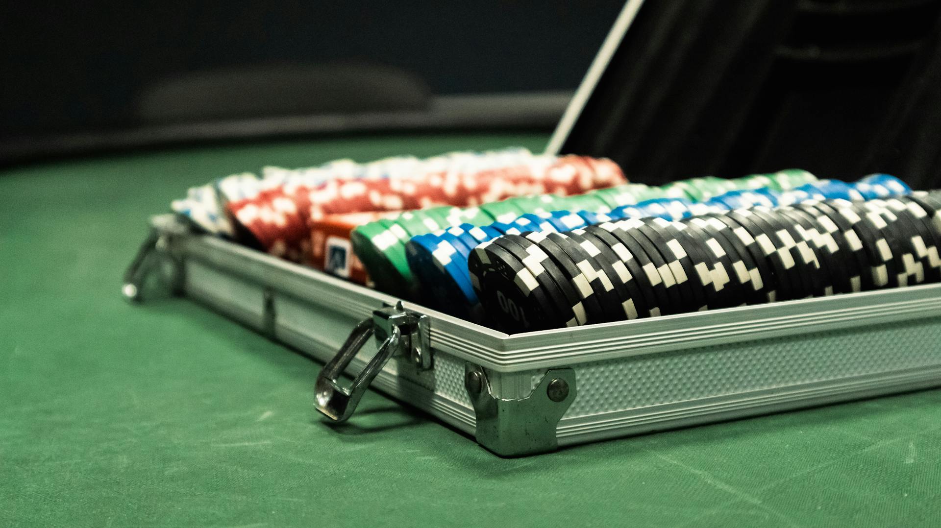 Close-up of a poker set with colorful chips arranged in a briefcase on a green table.