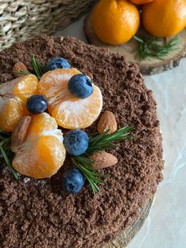 A close-up shot of a chocolate cake topped with tangerines, blueberries, almonds, and rosemary.