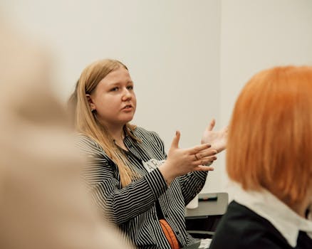 Woman with long blonde hair speaking passionately during a group meeting indoors.