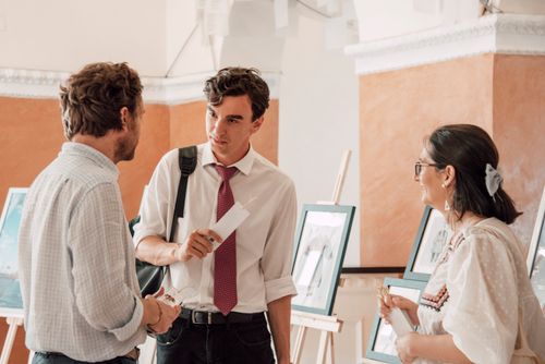 Free Three adults engaged in conversation at an art gallery exhibition with paintings on display. Stock Photo
