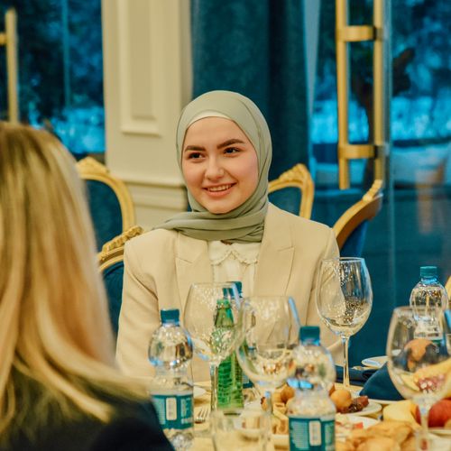 Free A woman in a headscarf smiles during an elegant dinner gathering, surrounded by fine dining table settings. Stock Photo