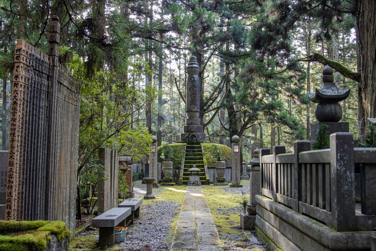 Stone lanterns and graves in Okunoin Cemetery, Koyasan, Japan, surrounded by towering ancient cedar trees