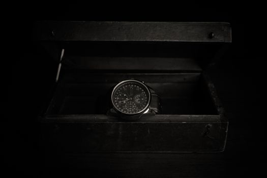 An elegant wristwatch inside an open black box, captured in a dark and moody setting.