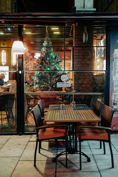 Cozy outdoor cafe setting at night with festive Christmas tree view.