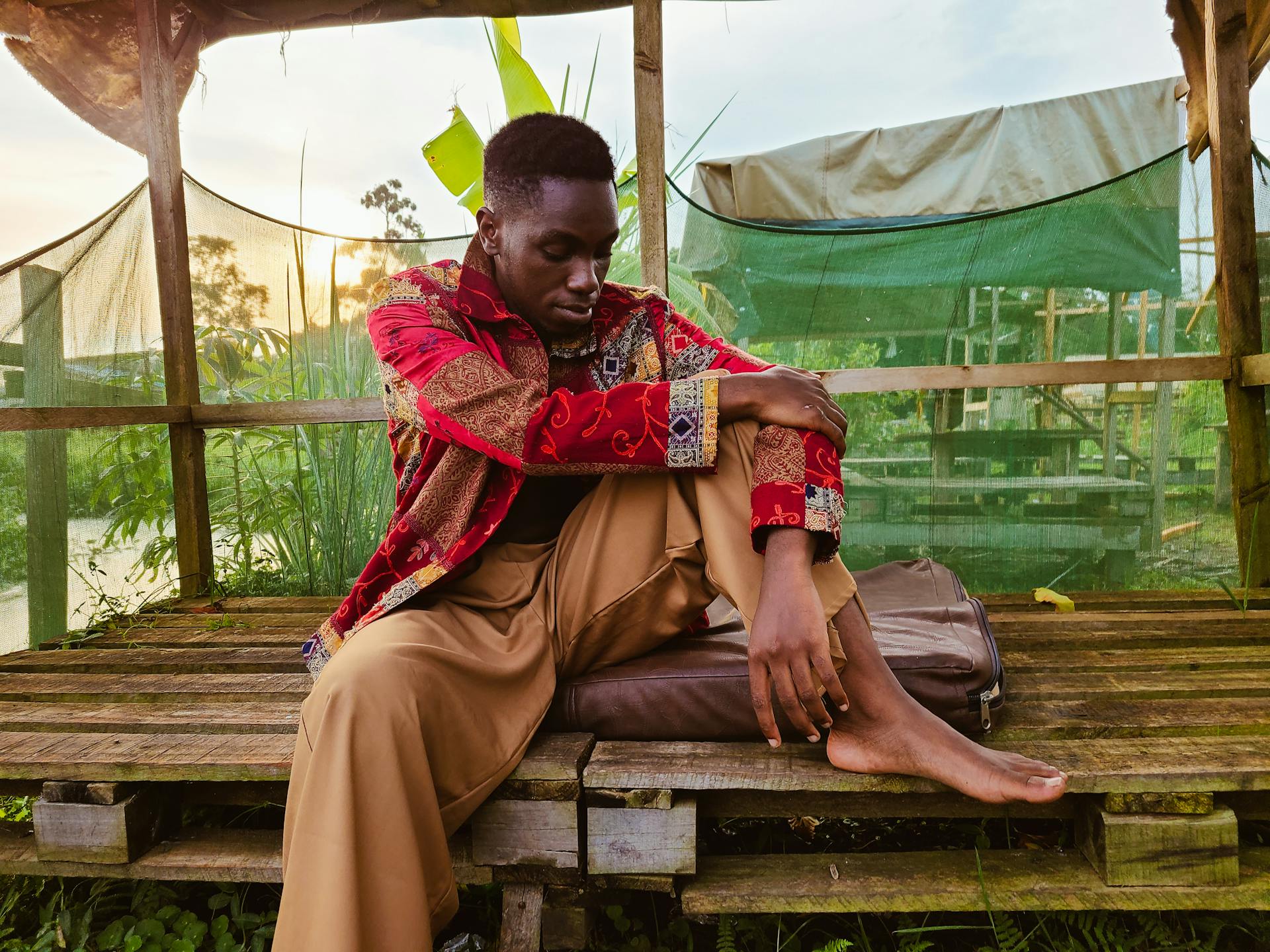 Man in traditional clothing sits thoughtfully on wooden pallets in Kampala, Uganda.
