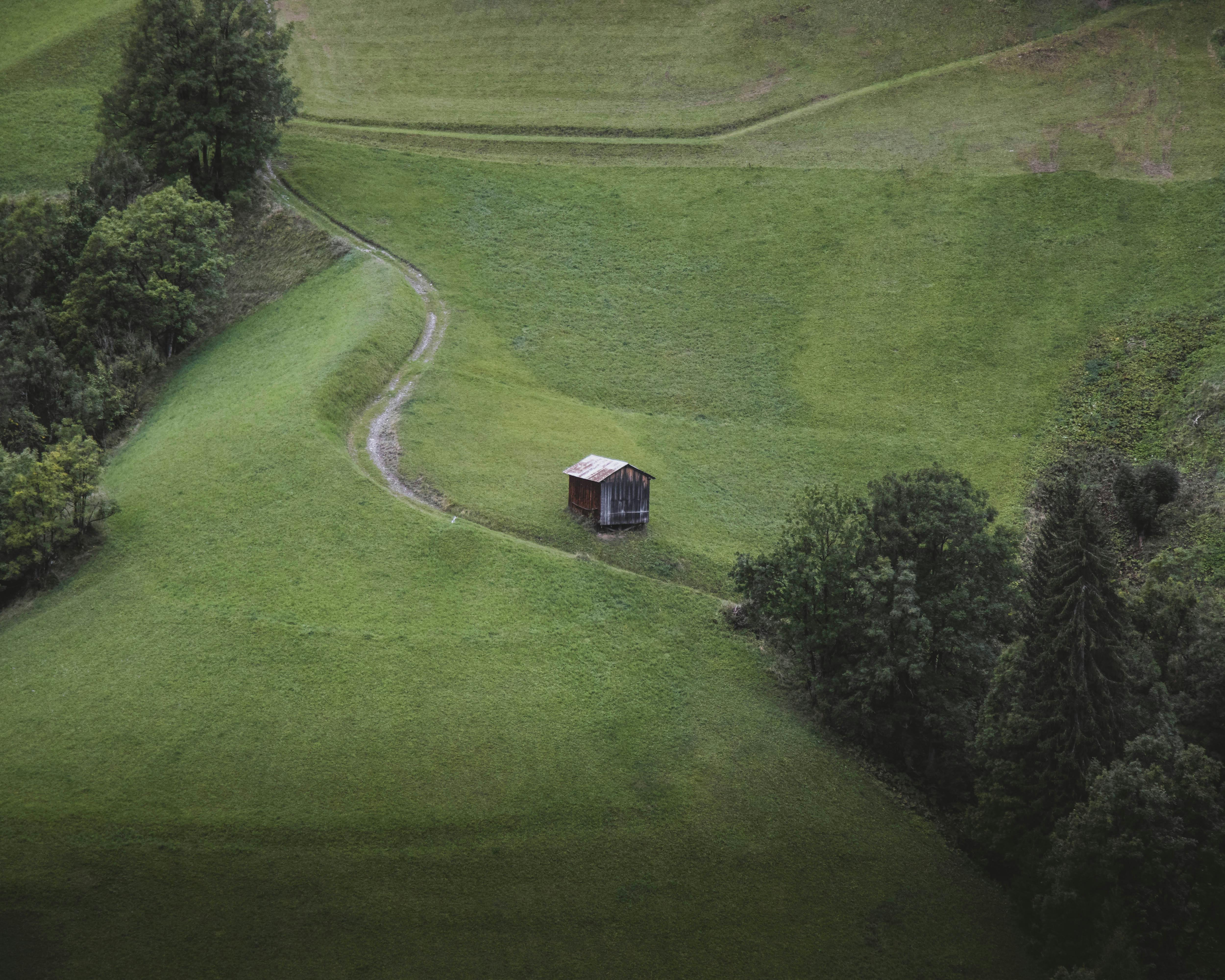Scenic aerial view of a solitary cabin amid lush green countryside with winding path.