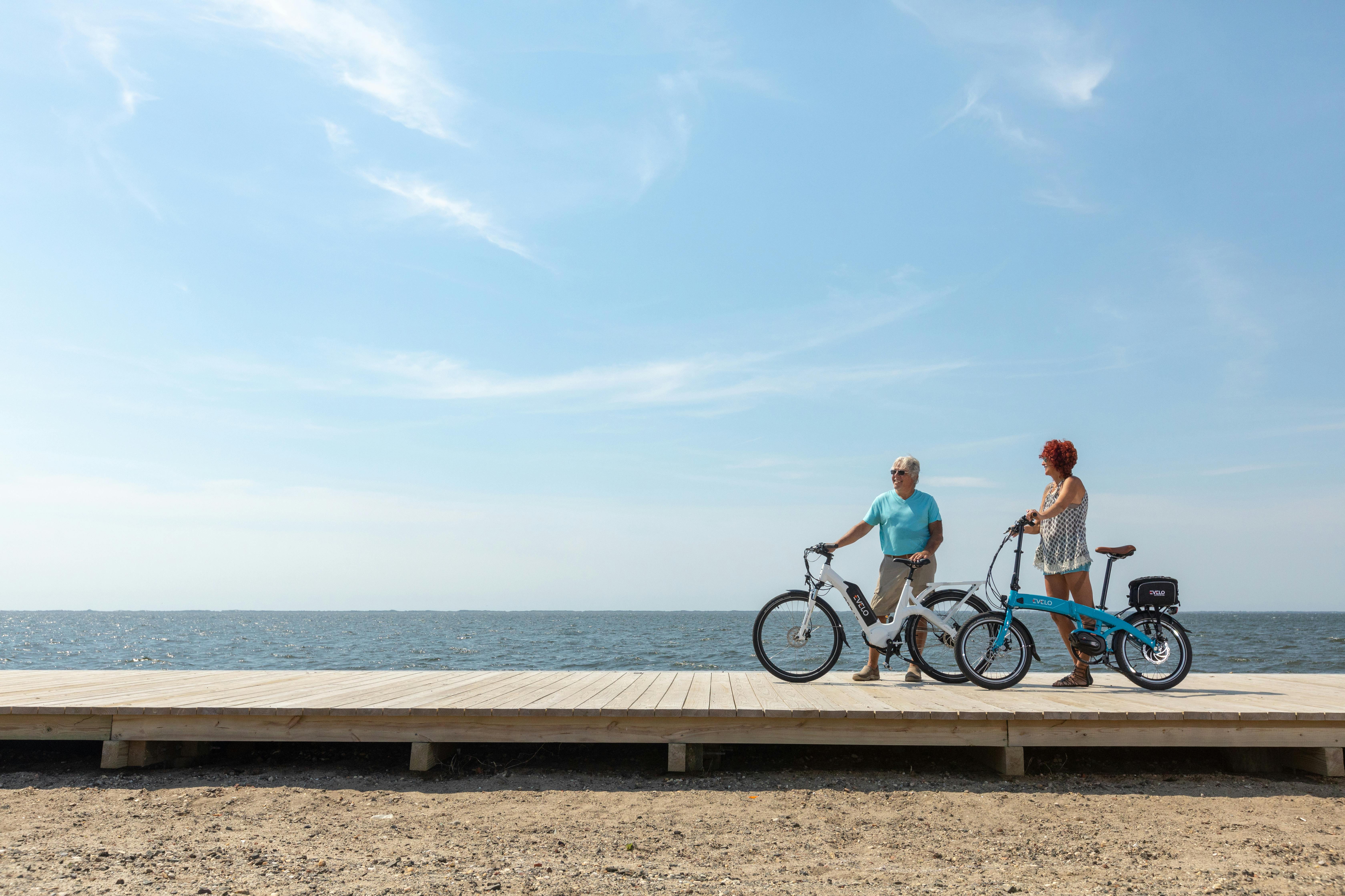two people on bicycles on a pier near the ocean