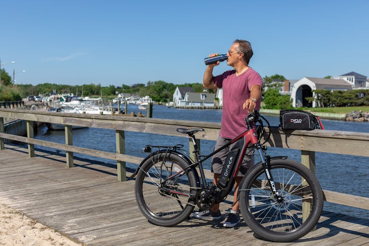 A Man Standing Beside A Bicycle Drinking From A Reusable Bottle 