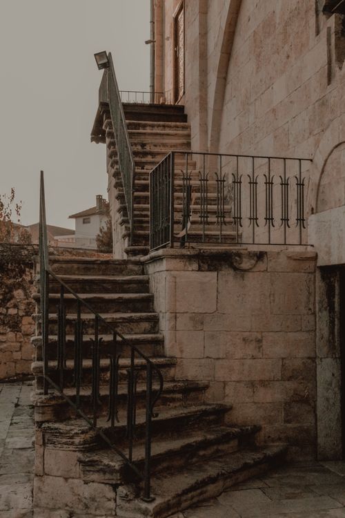 Free A vintage stone staircase with wrought iron railings leading to an ancient building outdoors. Stock Photo
