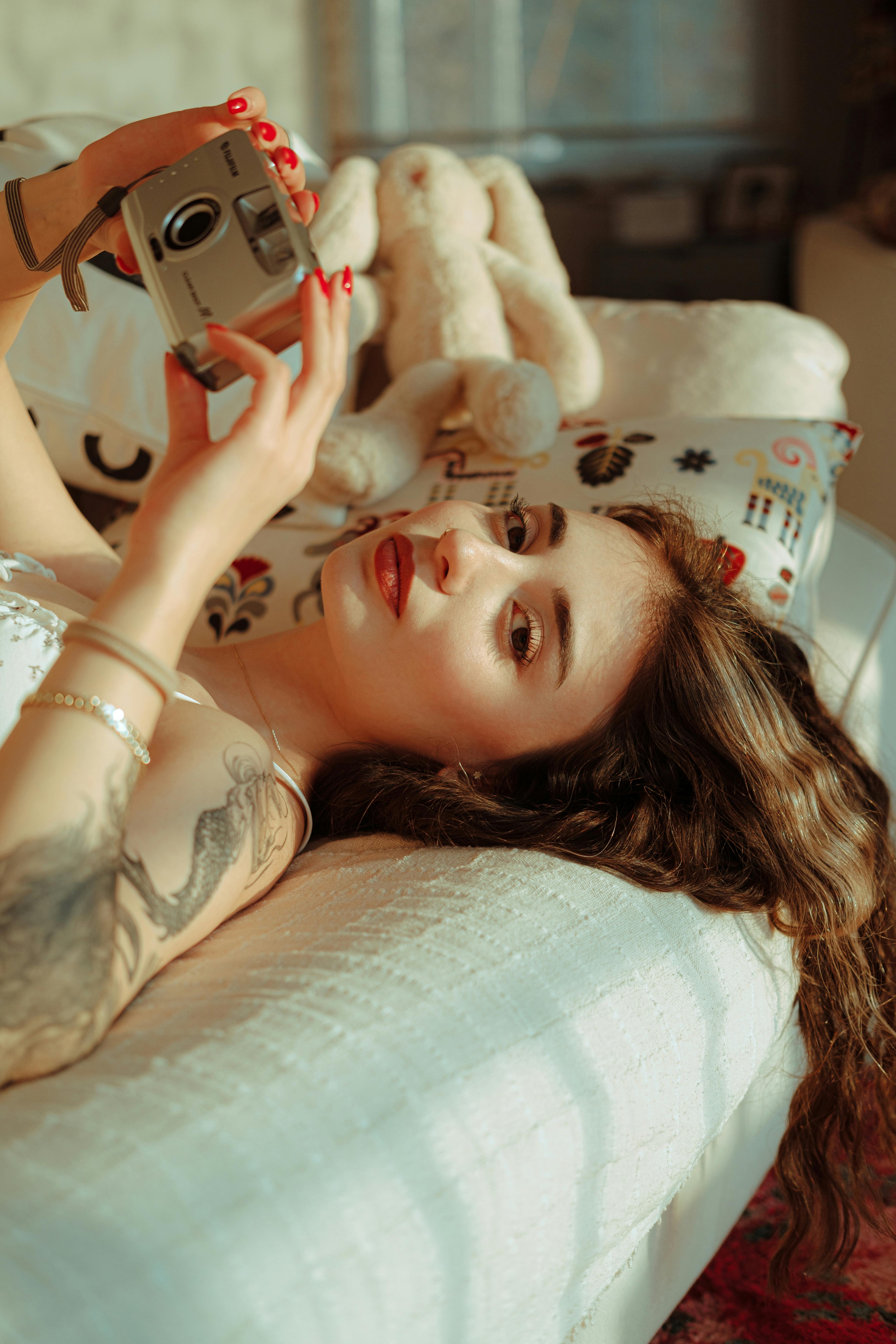 young woman lying on the bed and holding a camera