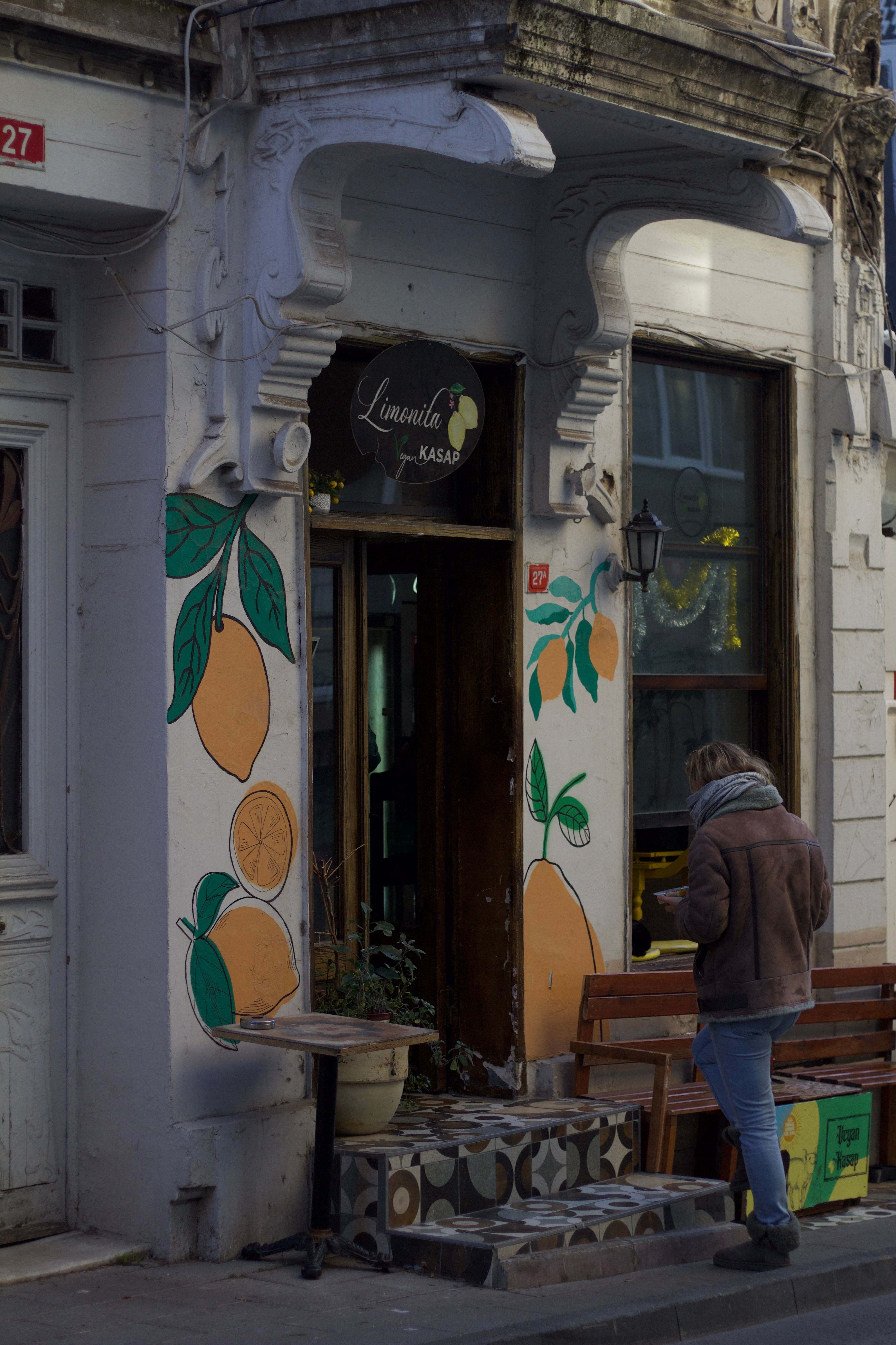 Person walking into a café with vibrant lemon murals, urban setting.