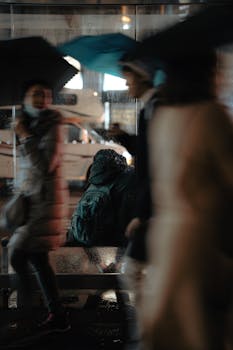 Blurry pedestrians with umbrellas at night in a city, highlighting urban rain scene.